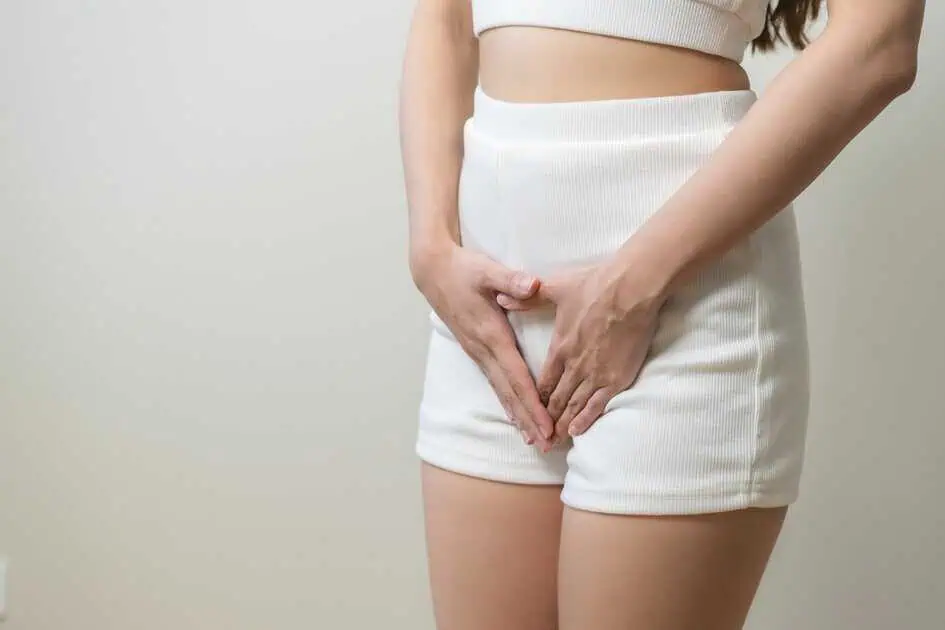 Woman in white shorts with hands over lower abdomen, symbolizing ThermiVa vaginal wellness treatment in Cornelius, NC